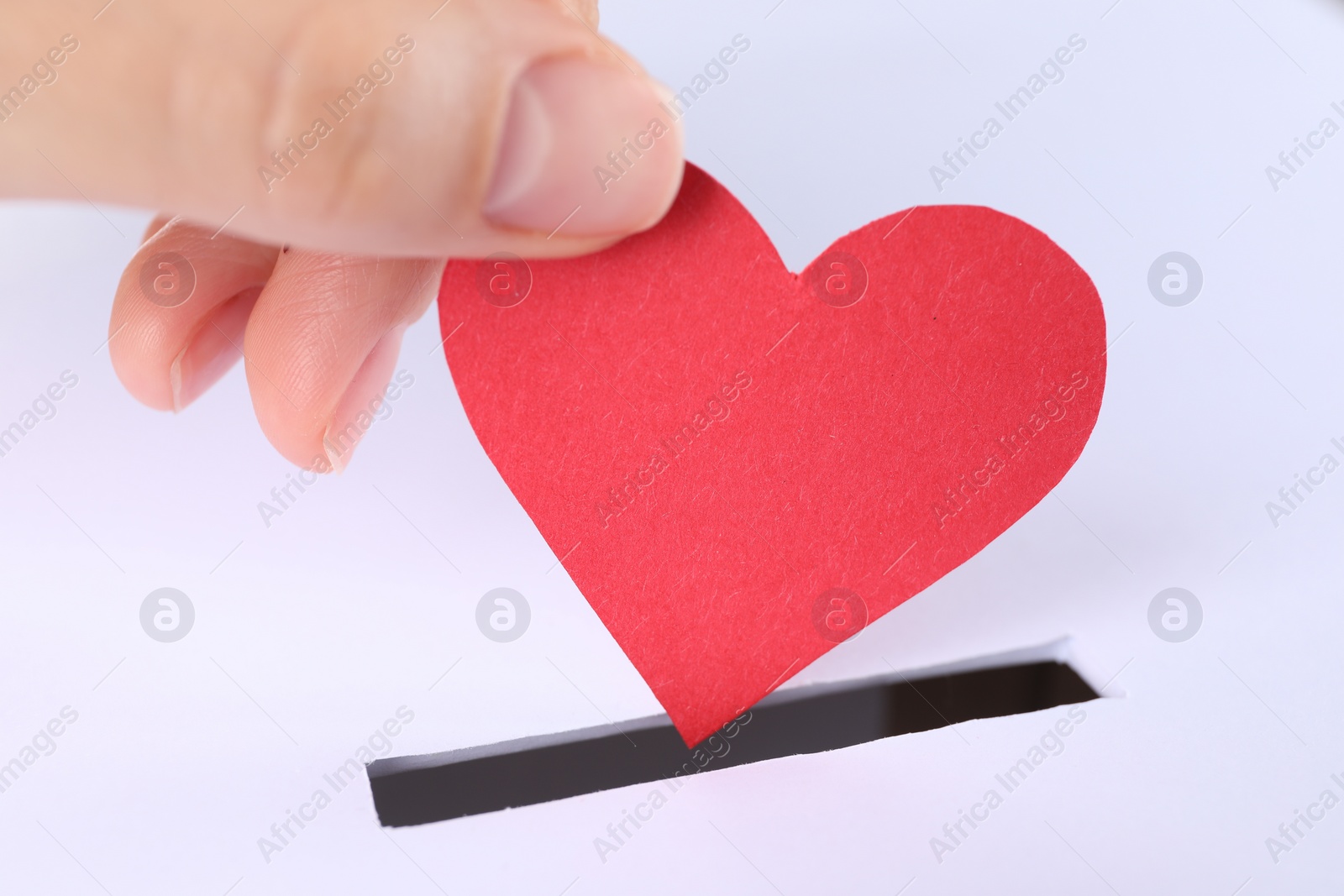 Photo of Woman putting red heart into slot of donation box, closeup