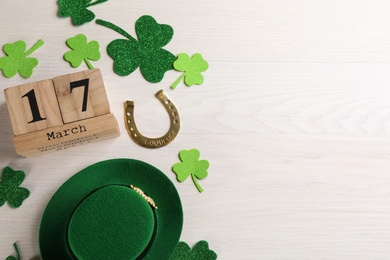 Photo of Flat lay composition with leprechaun hat and block calendar on white wooden table, space for text. St Patrick's Day celebration
