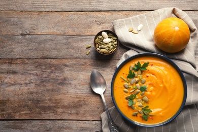 Photo of Flat lay composition with pumpkin cream soup in bowl on wooden background. Space for text