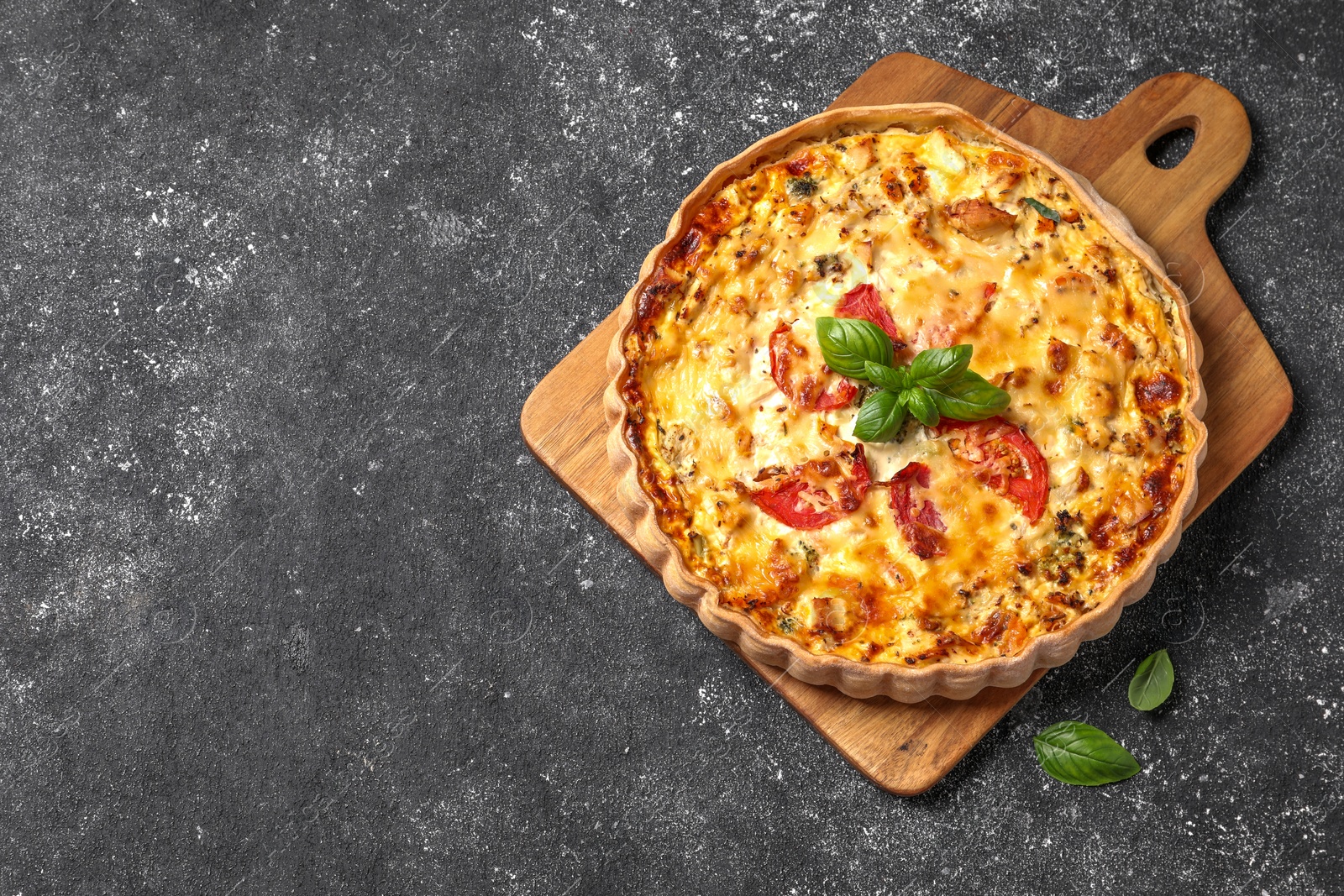 Photo of Tasty quiche with tomatoes, basil and cheese on dark textured table, top view. Space for text