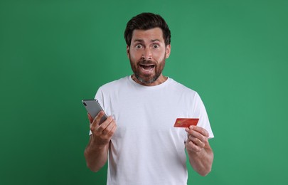Photo of Shocked man with smartphone and credit card on green background. Be careful - fraud
