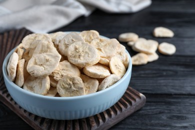 Photo of Bowl with dried banana slices on black wooden table, closeup