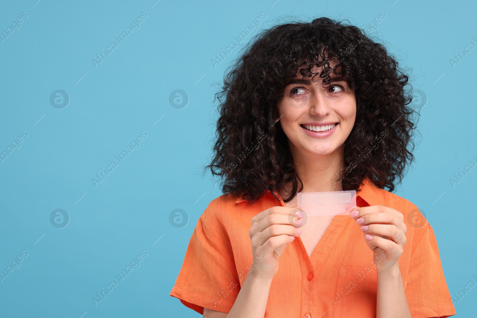 Photo of Young woman holding teeth whitening strips on light blue background, space for text