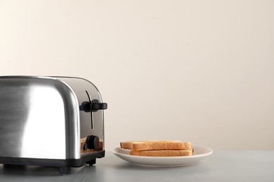 Photo of Electric toaster with bread slices on light table. Space for text