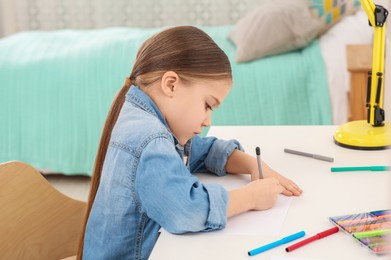 Cute little girl drawing with markers at desk in room. Home workplace