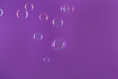 Beautiful transparent soap bubbles on violet background, space for text