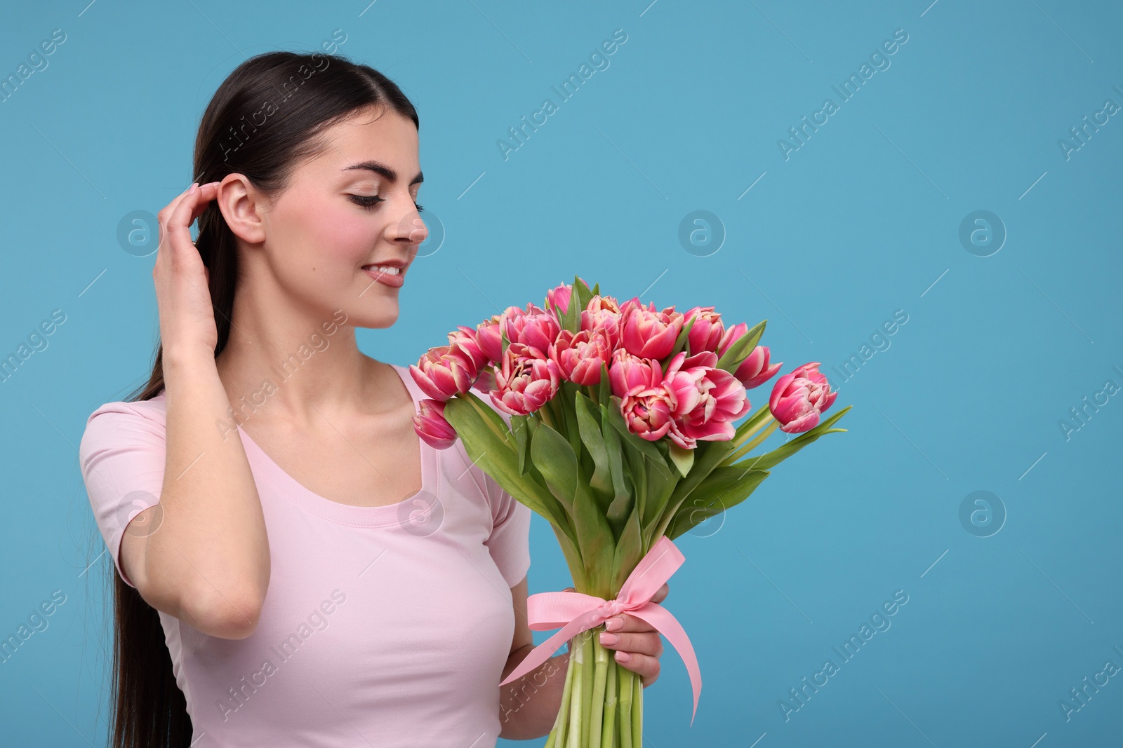 Photo of Happy young woman with beautiful bouquet on light blue background