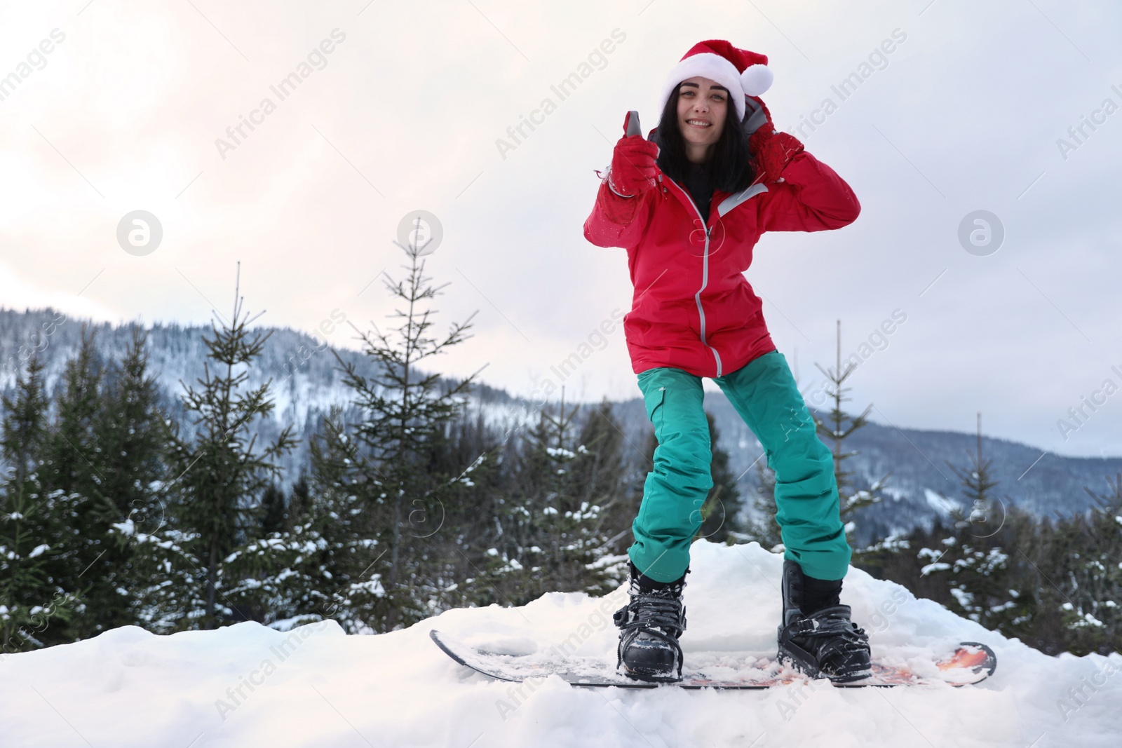 Photo of Young snowboarder wearing Santa hat on snowy hill. Winter vacation