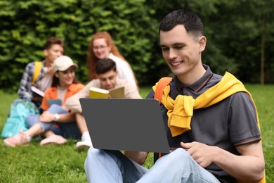 Students learning together in park. Happy young man working with laptop on green grass, selective focus