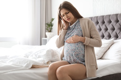 Photo of Young pregnant woman suffering from headache at home