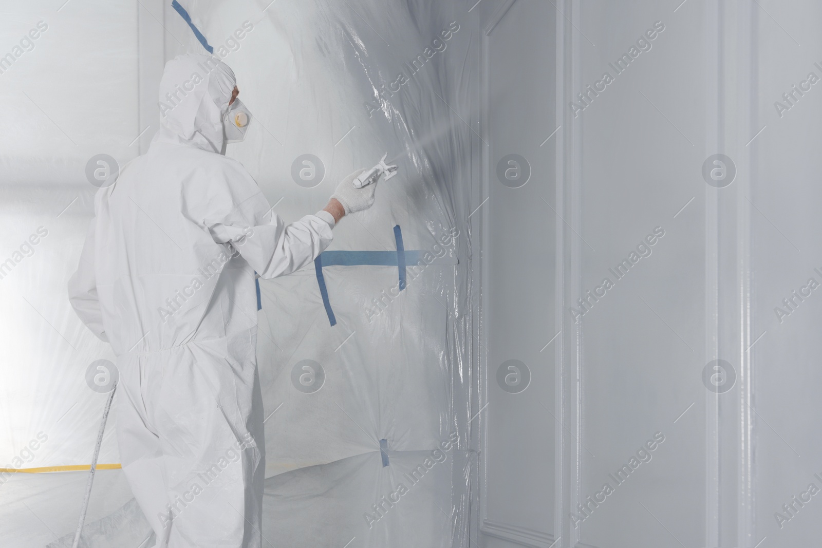 Photo of Decorator dyeing wall in grey color with spray paint, space for text