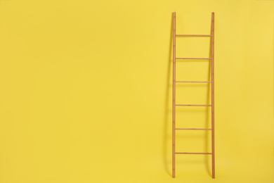 Photo of Modern wooden ladder on yellow background. Space for text