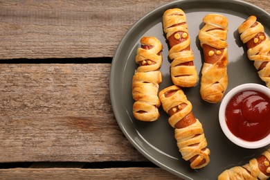 Photo of Cute sausage mummies served with ketchup on wooden table, top view with space for text. Halloween party food