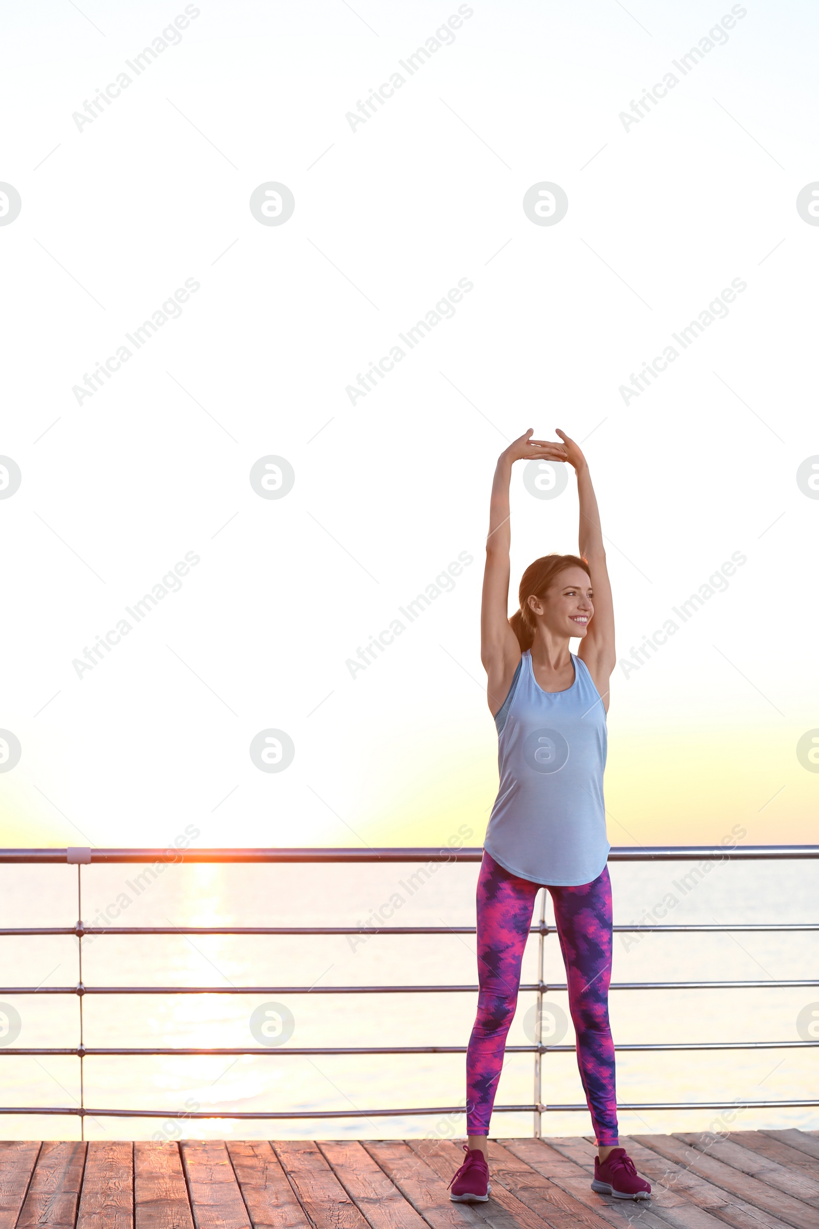 Photo of Young woman doing fitness exercises on pier in morning