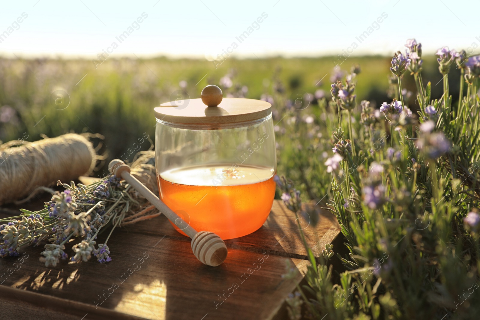 Photo of Jar of honey on wooden table in lavender field