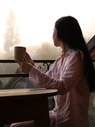 Photo of Young woman sitting at table on balcony with cup of tea in morning