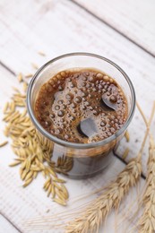 Photo of Cup of barley coffee, grains and spikes on white wooden table, above view