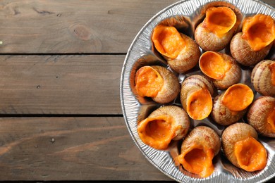 Photo of Delicious cooked snails on wooden table, top view. Space for text