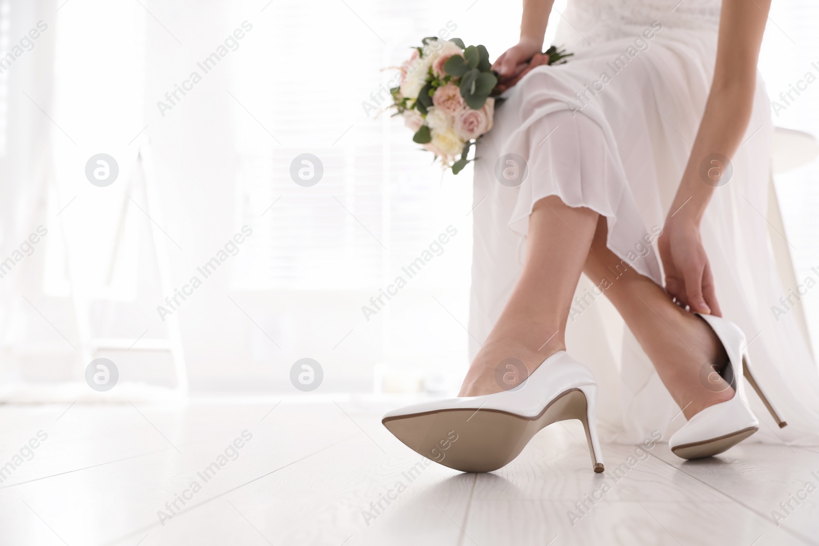 Photo of Young bride putting on beautiful wedding shoes indoors, closeup. Space for text