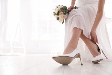 Young bride putting on beautiful wedding shoes indoors, closeup. Space for text