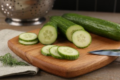 Photo of Cucumbers, knife, cutting board and dill on wooden table, closeup
