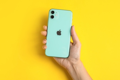 Photo of MYKOLAIV, UKRAINE - JULY 10, 2020: Woman holding new modern Iphone 11 Green on yellow background, top view