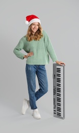 Young woman in Santa hat with synthesizer on light grey background. Christmas music