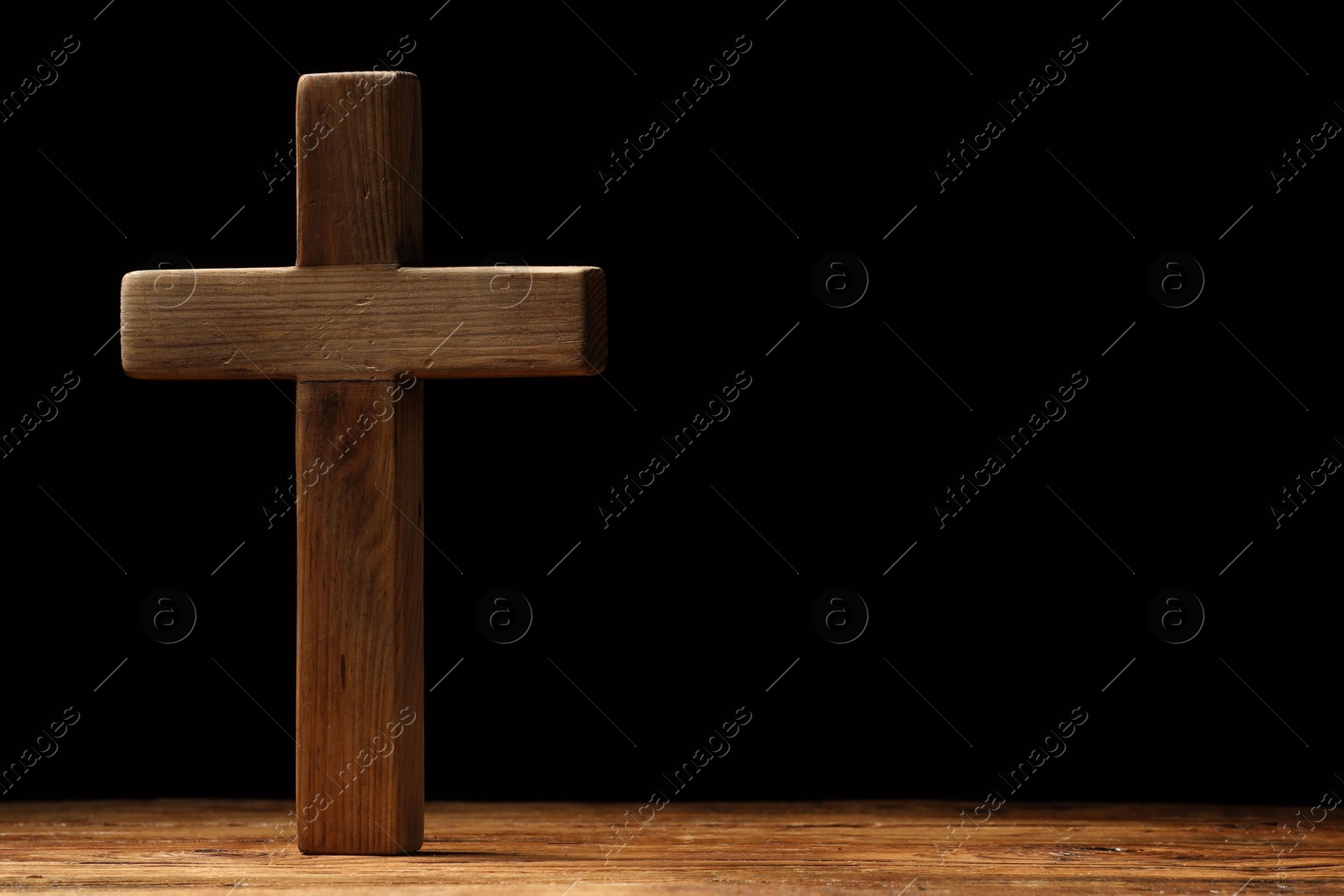 Photo of Cross on wooden table against black background, space for text. Religion of Christianity