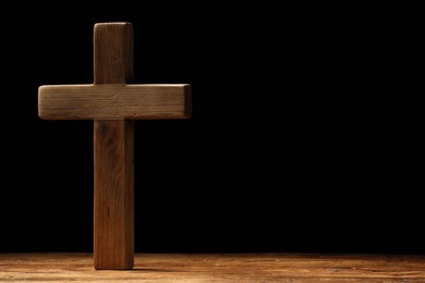 Photo of Cross on wooden table against black background, space for text. Religion of Christianity