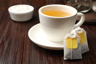 Tea bags and cup of hot beverage on wooden table, closeup. Space for text