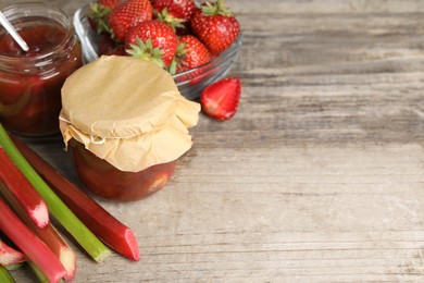 Photo of Tasty rhubarb jam, stems and strawberries on wooden table. Space for text