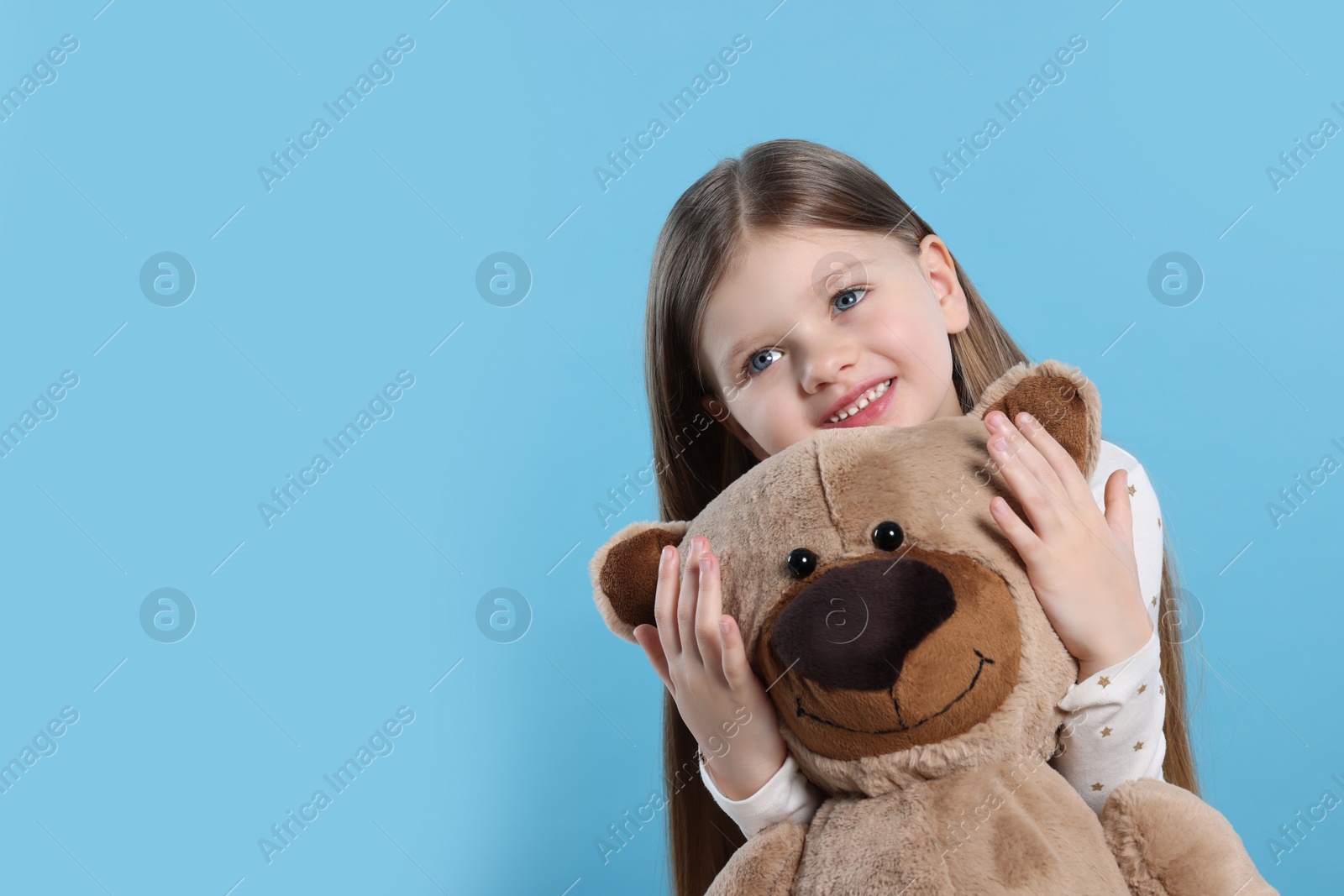 Photo of Cute little girl with teddy bear on light blue background. Space for text