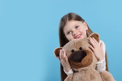 Cute little girl with teddy bear on light blue background. Space for text
