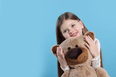 Photo of Cute little girl with teddy bear on light blue background. Space for text