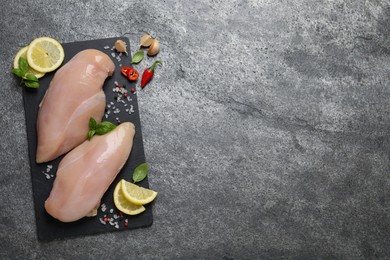 Photo of Raw chicken breasts and ingredients on grey table, flat lay. Space for text