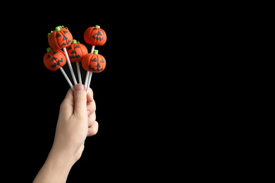 Photo of Woman with delicious pumpkin shaped cake pops and space for text on black background, closeup. Halloween celebration