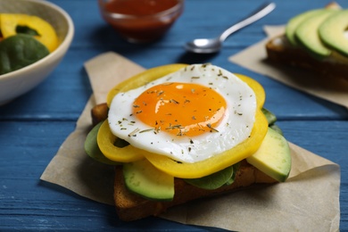 Photo of Tasty toast with fried egg, bell pepper and avocado on blue wooden table, closeup