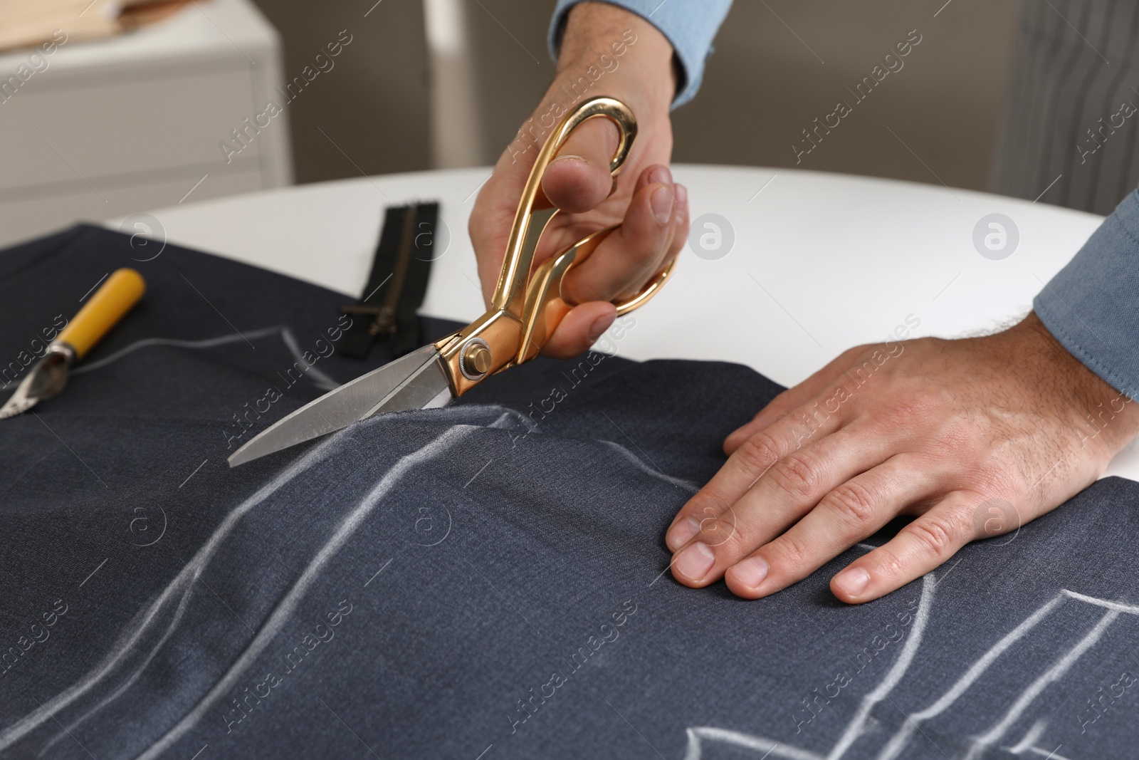 Photo of Tailor cutting fabric with scissors at table in atelier, closeup