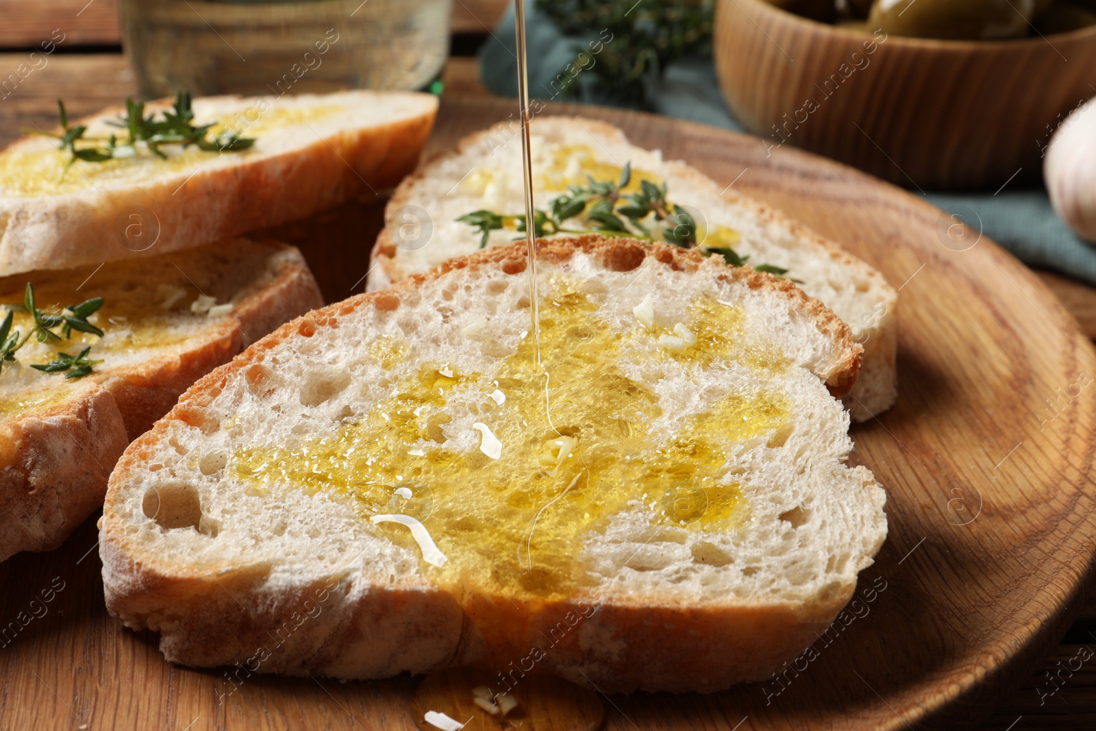 Photo of Pouring oil onto slice of bread on wooden plate, closeup