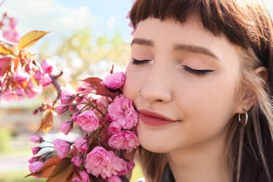 Beautiful young woman near blossoming sakura tree in park, closeup