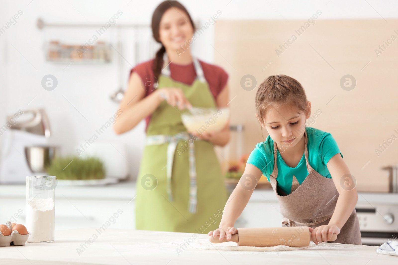 Photo of Mother and her daughter making dough at table in kitchen