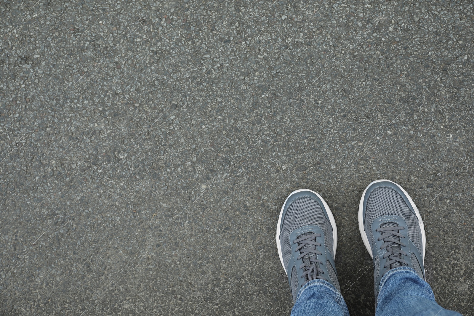 Photo of Man in sneakers standing on asphalt, top view. Space for text