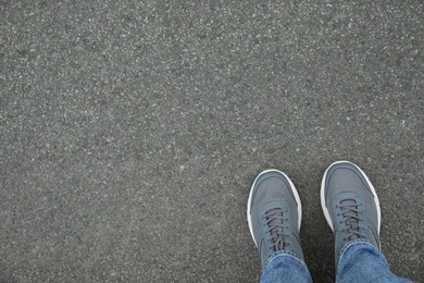 Man in sneakers standing on asphalt, top view. Space for text