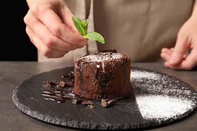 Chef decorating delicious fresh chocolate fondant with mint at table. Lava cake recipe