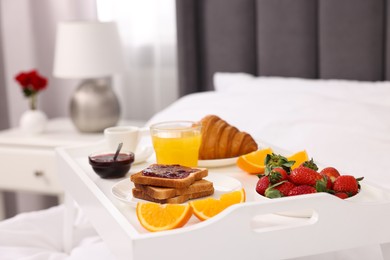 Photo of Tray with delicious breakfast on bed in room, closeup.