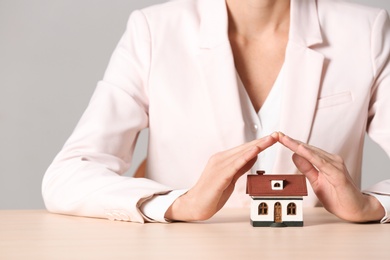 Female agent covering house model at table, closeup. Home insurance