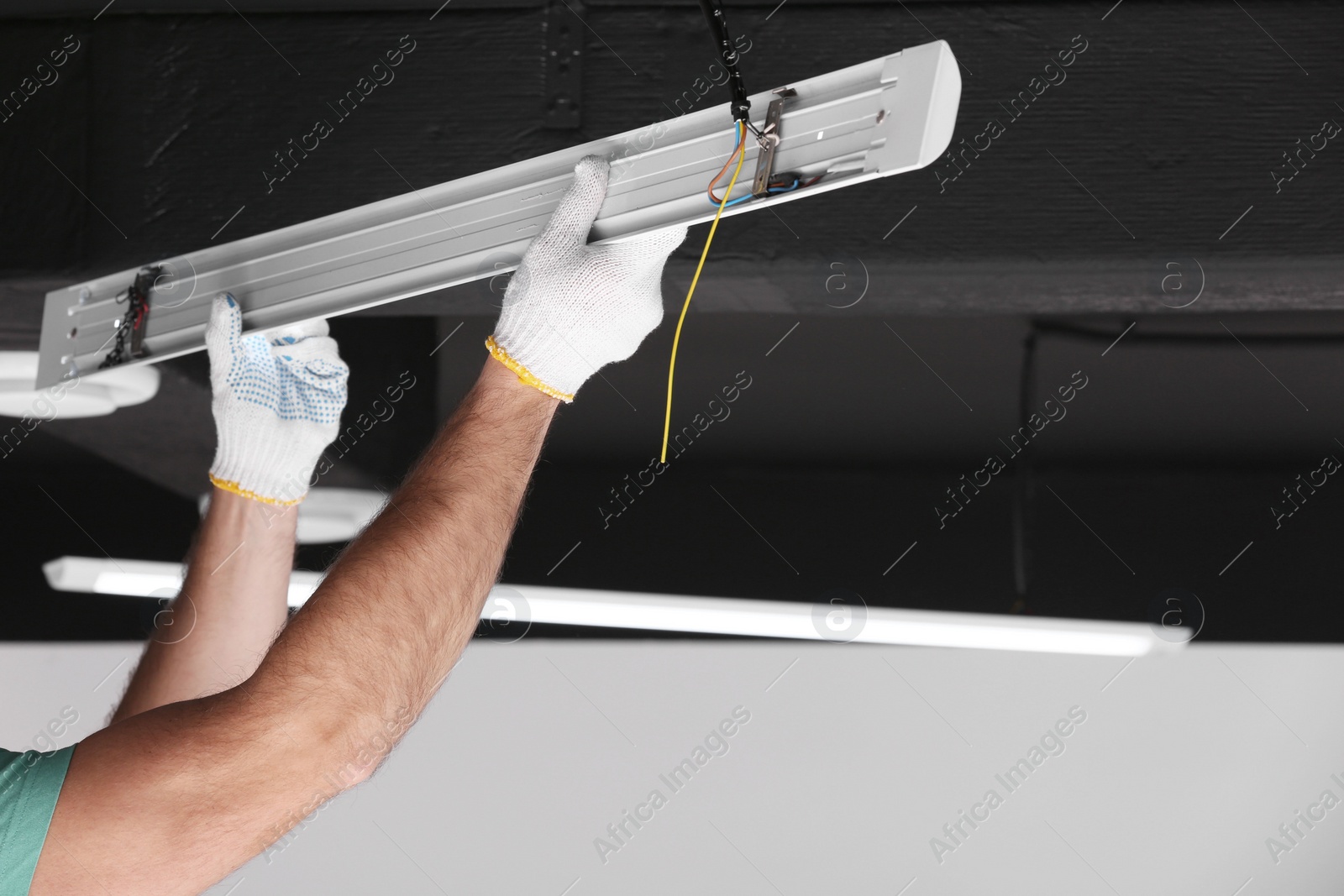 Photo of Ceiling light. Electrician installing led linear lamp indoors, closeup. Space for text