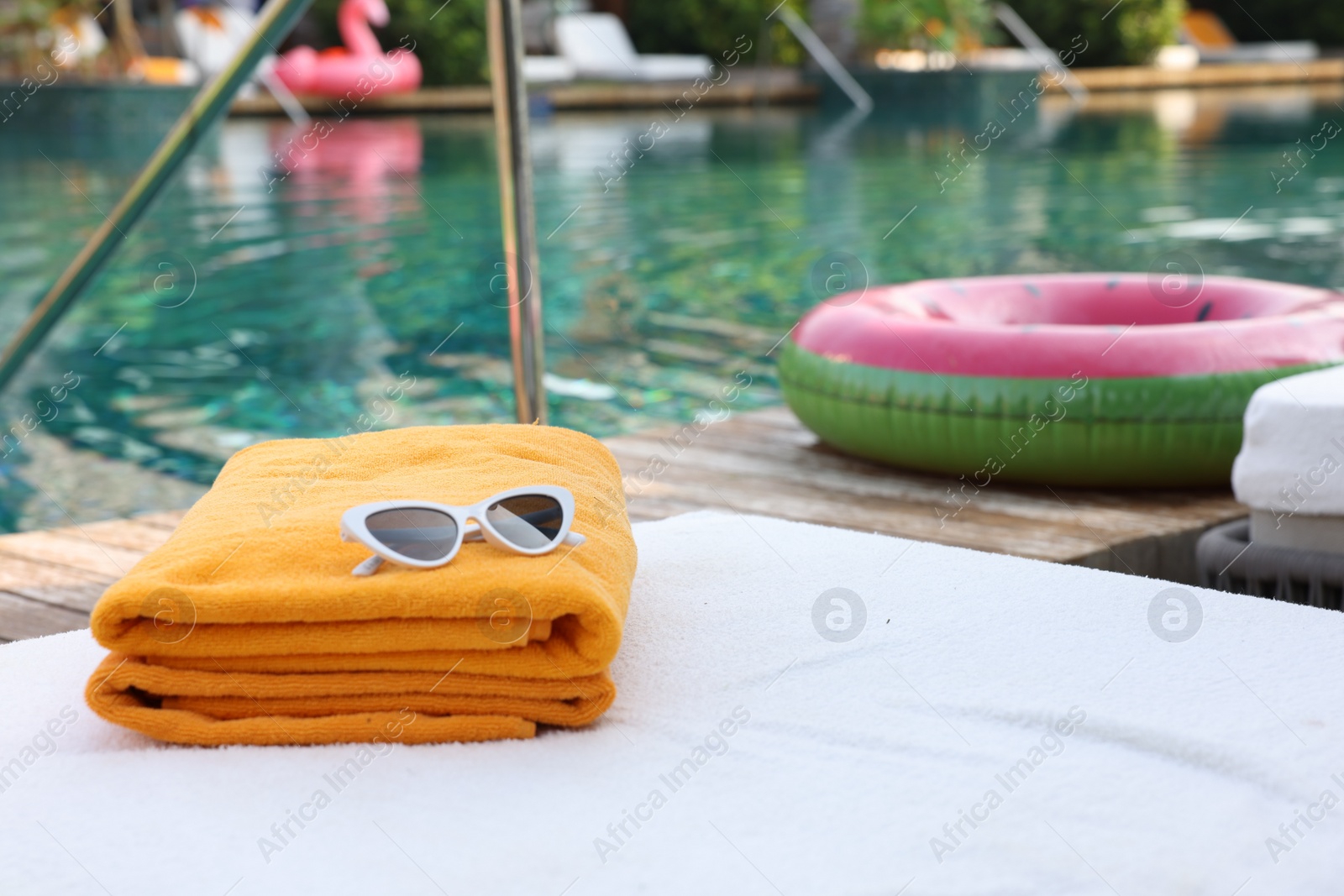 Photo of Beach towels and sunglasses on sun lounger near outdoor swimming pool, space for text. Luxury resort