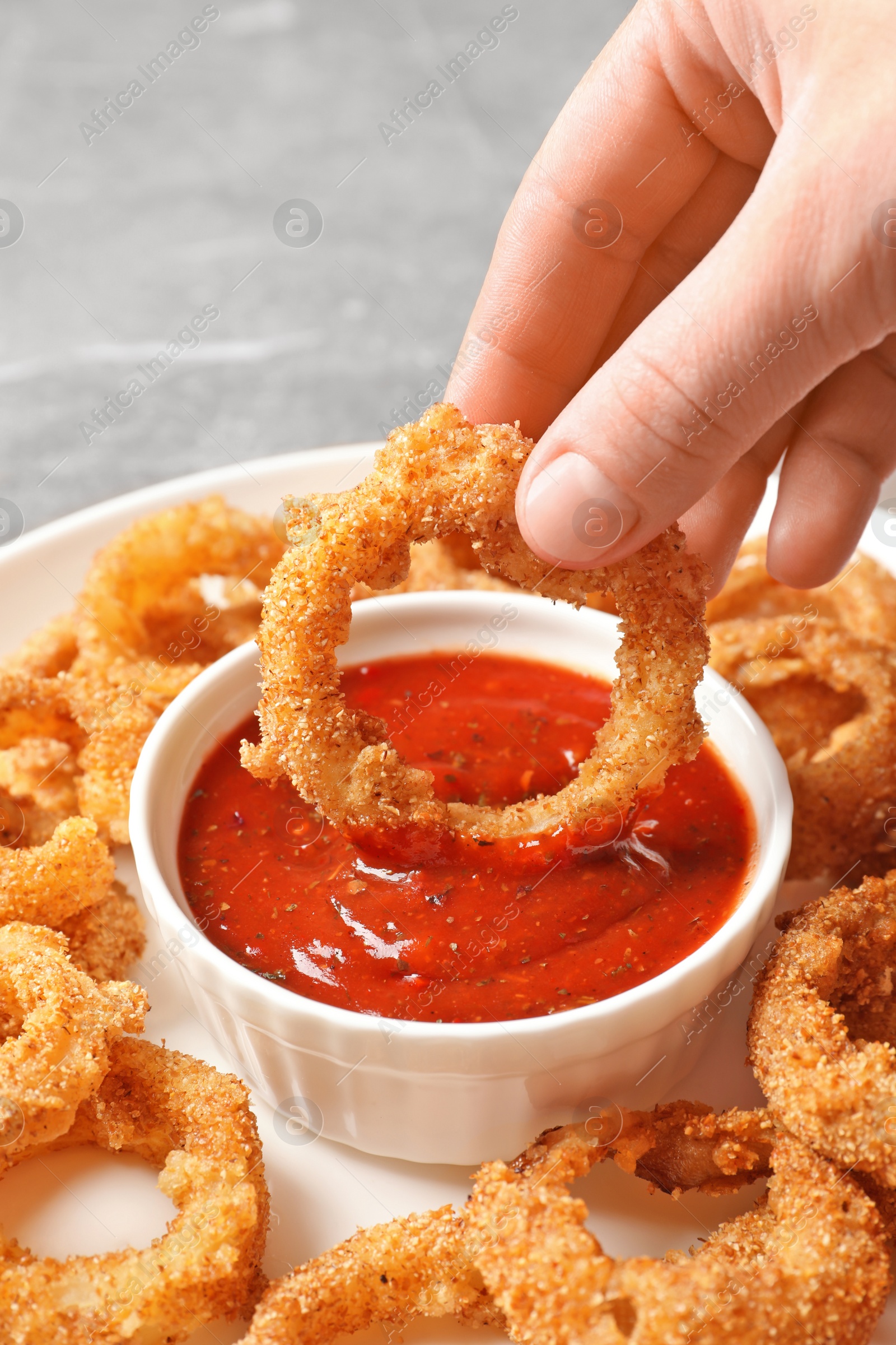 Photo of Woman dipping crunchy fried onion ring in tomato sauce, closeup
