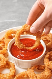 Photo of Woman dipping crunchy fried onion ring in tomato sauce, closeup